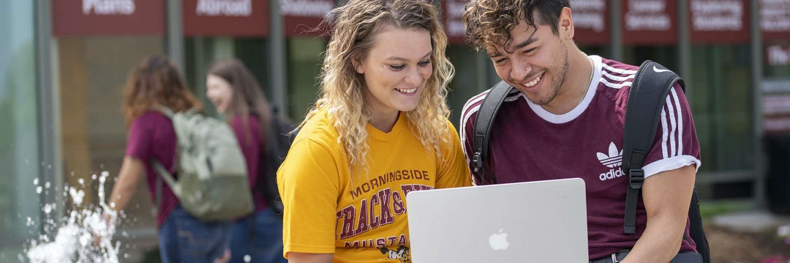 Students look at laptop outside by fountain